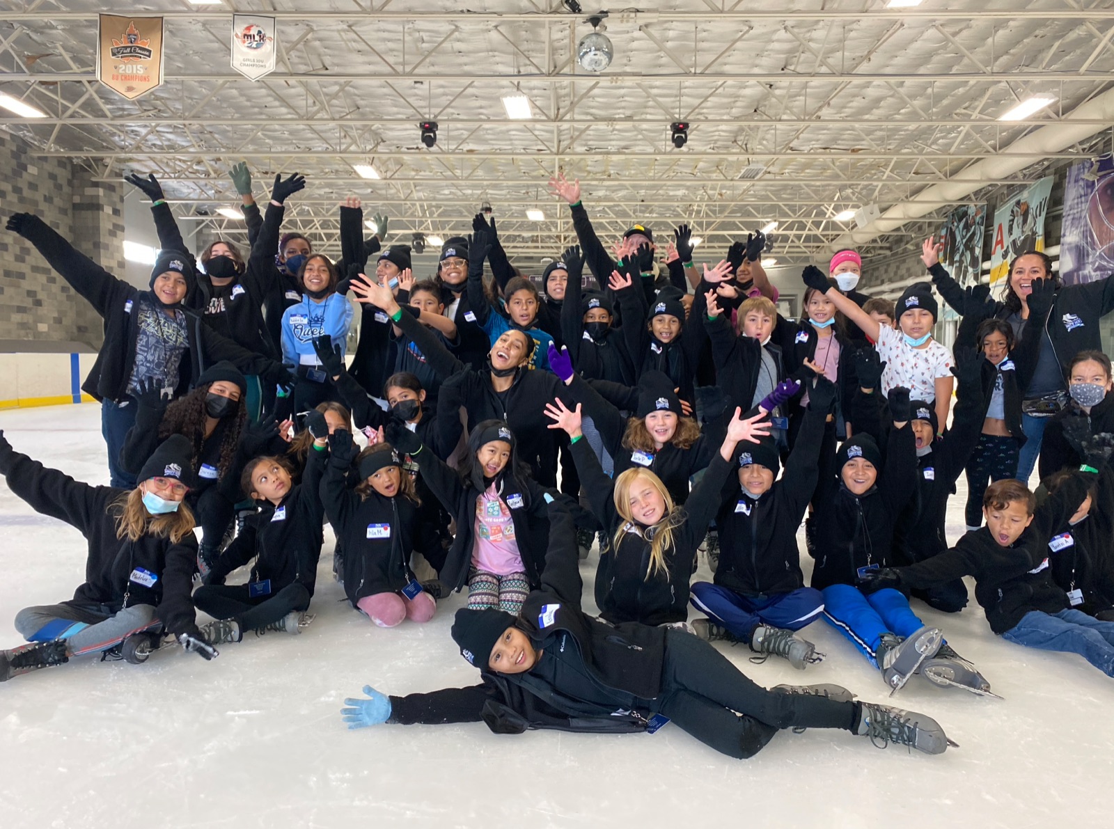 A large group of Unity Ice Academy skaters cheer with their arms raised on the ice.