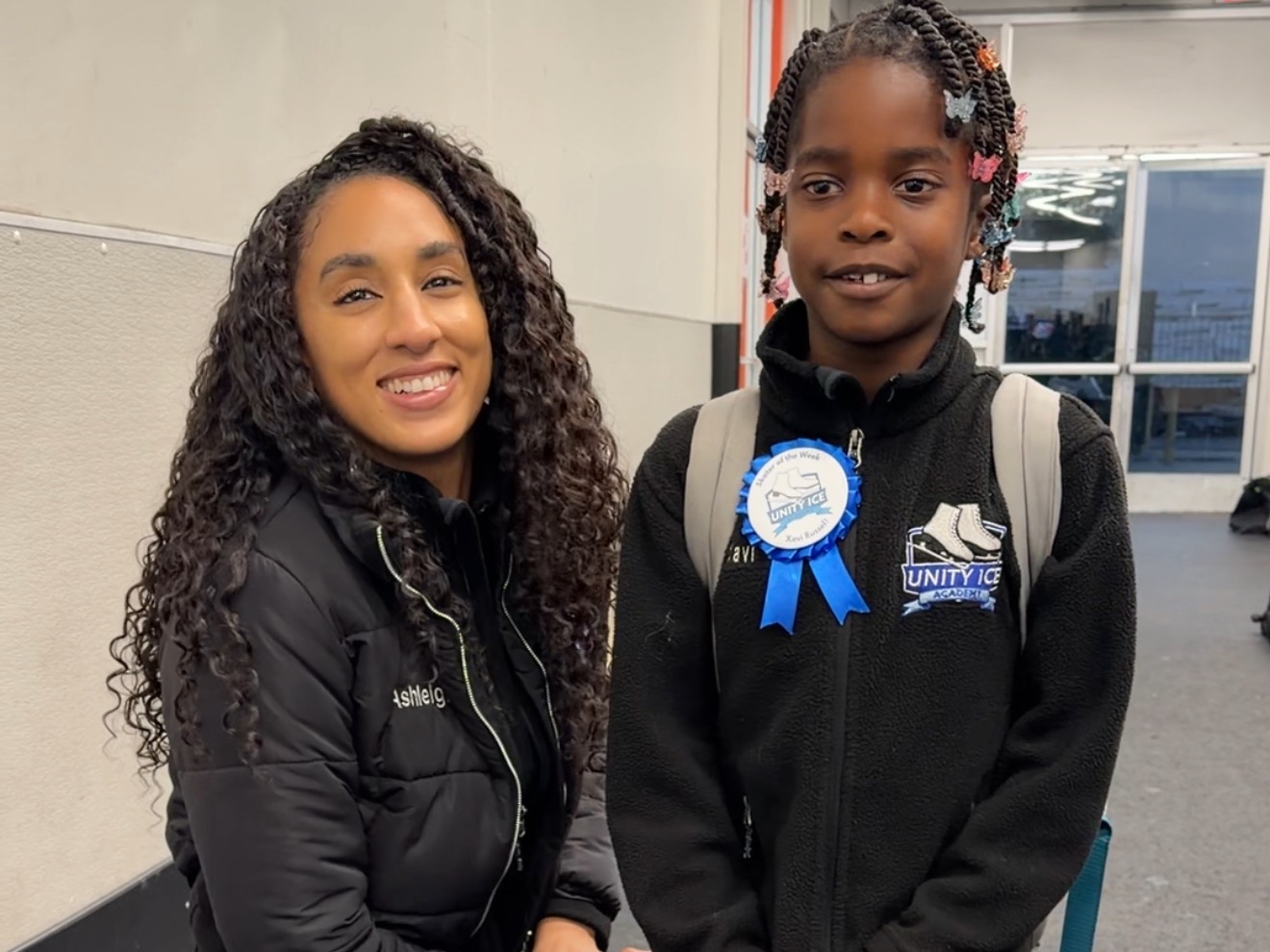 Ashleigh Ellis smiles beside a young skater wearing a Unity Ice Academy jacket and a blue award ribbon.