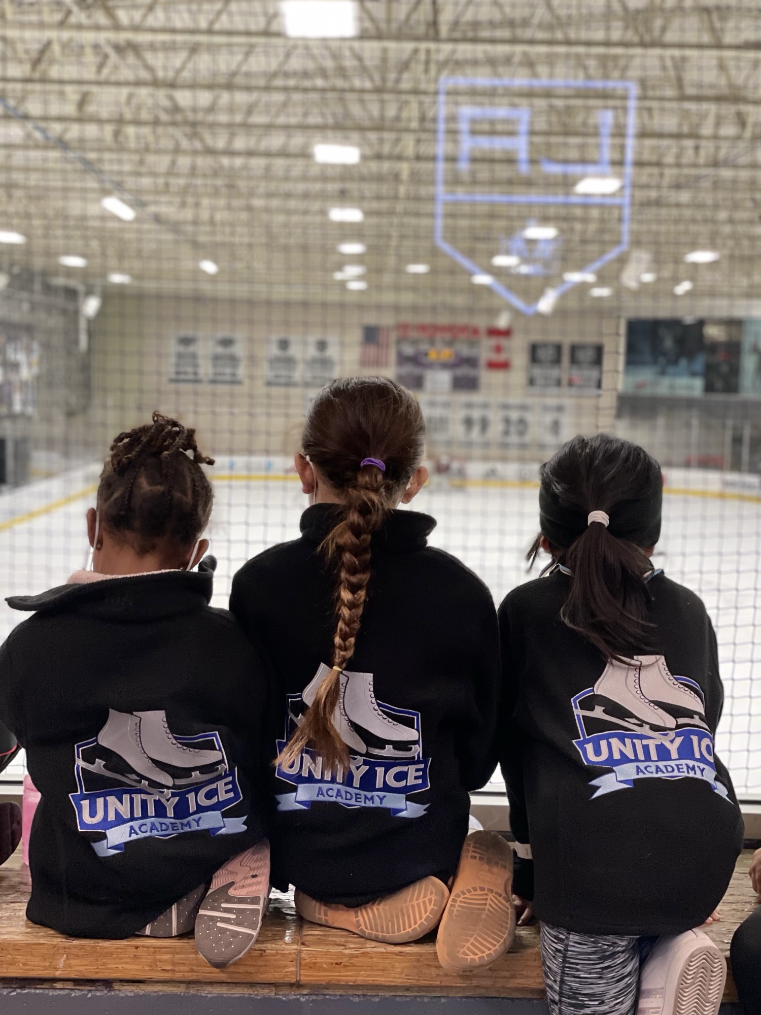 Three young skaters in Unity Ice Academy jackets stand together at the rink.