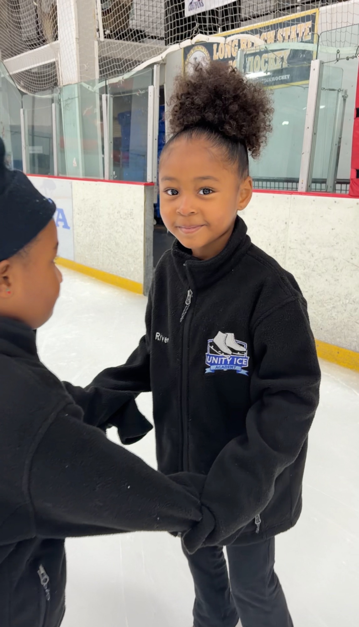 A smiling young skater in a Unity Ice Academy jacket at the rink.